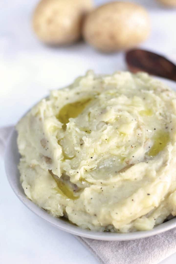 closeup of creamy mashed potatoes with wooden spoon and raw potatoes in background