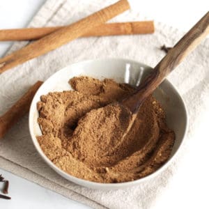 pumpkin pie spice is stirred in a shallow dish with a wooden spoon