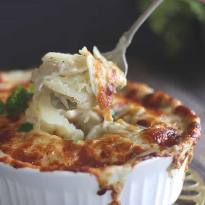 closeup of forkful of creamy scalloped potatoes lifted from melted, browned, cheese surface