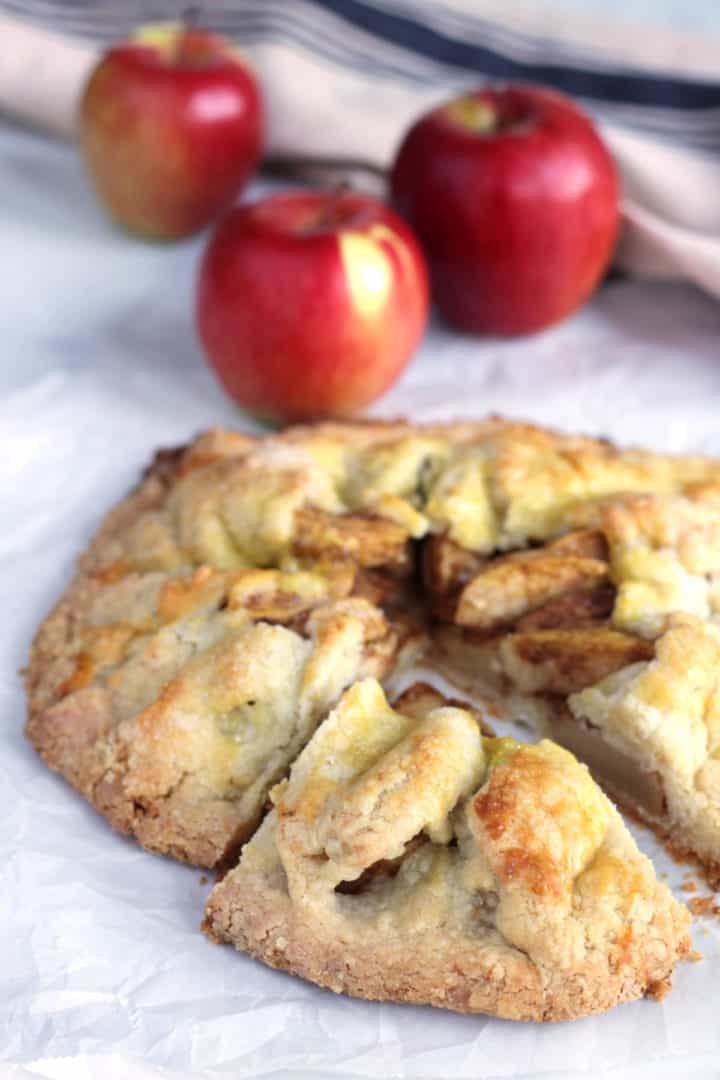 galette in parchment paper with a slice pulled out and fresh apples in background