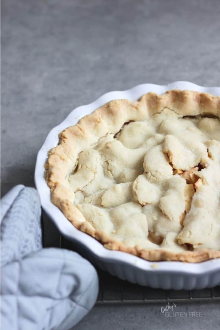 looking down from an angle on a baked pie crust with golden edges in a white pan with a quilted grey oven mitt