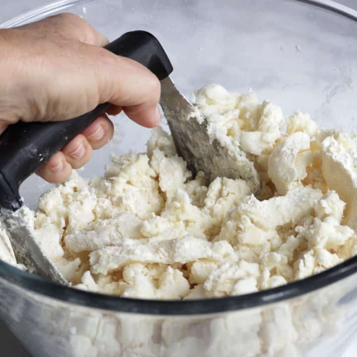 a hand working pastry blender into a lumpy flour mixture