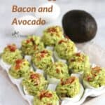 deviled eggs sprinkled with bacon in white dish, avocado and two whole eggs in background