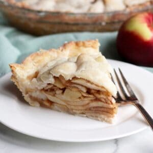 piece of apple pie filled with sliced apples on white plate with silver fork