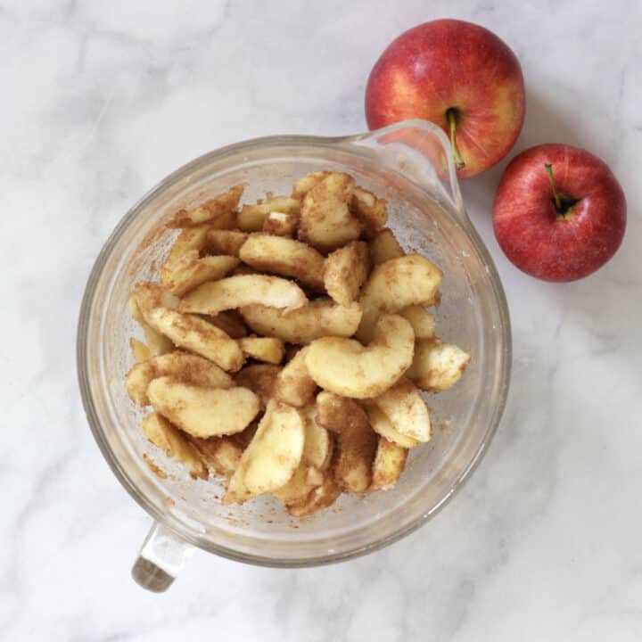 apples slices tossed in sugar and cinnamon in glass bowl