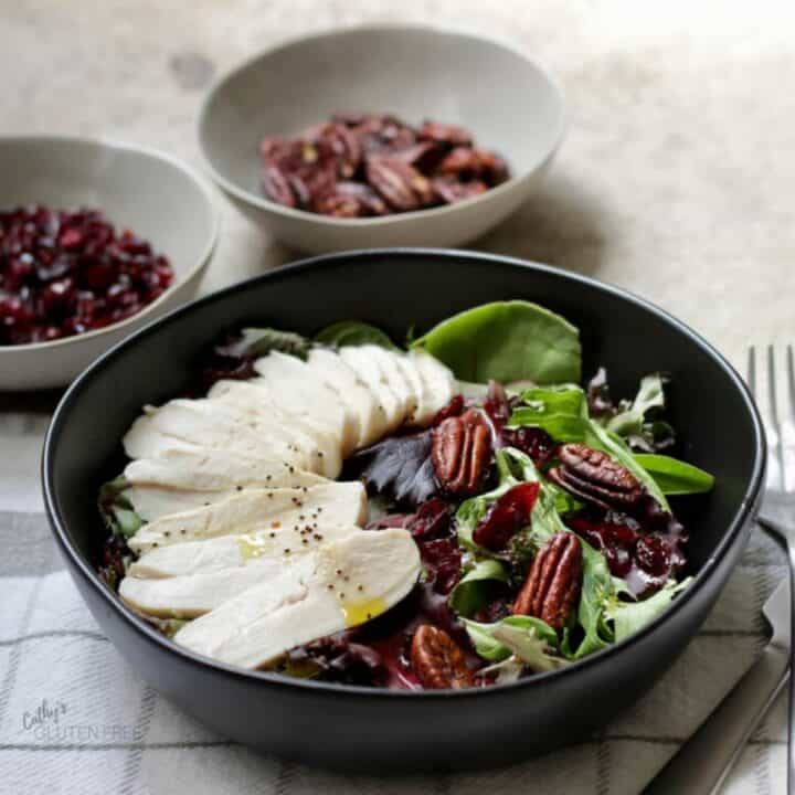 sliced, cooked turkey, dried cranberries, and pecans on a bed of fresh lettuce in black bowl