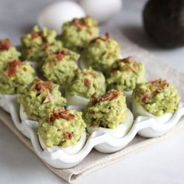 green deviled eggs garnished with chopped bacon in a white dish