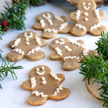 gingerbread men scattered randomly on white marble interspersed with evergreen sprigs