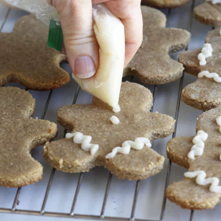 Icing being squeezed from the corner of a plastic bag into dots and lines on cookies