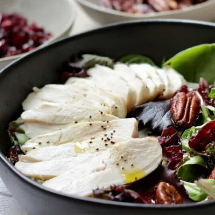 cooked turkey slices sit on top of a salad in a black bowl