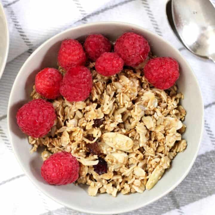 granola with raspberries on top in light grey bowl