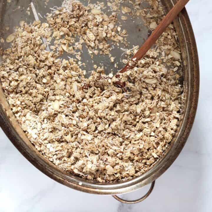 wooden spoon stirring oat mixture in stainless steel roasting pan