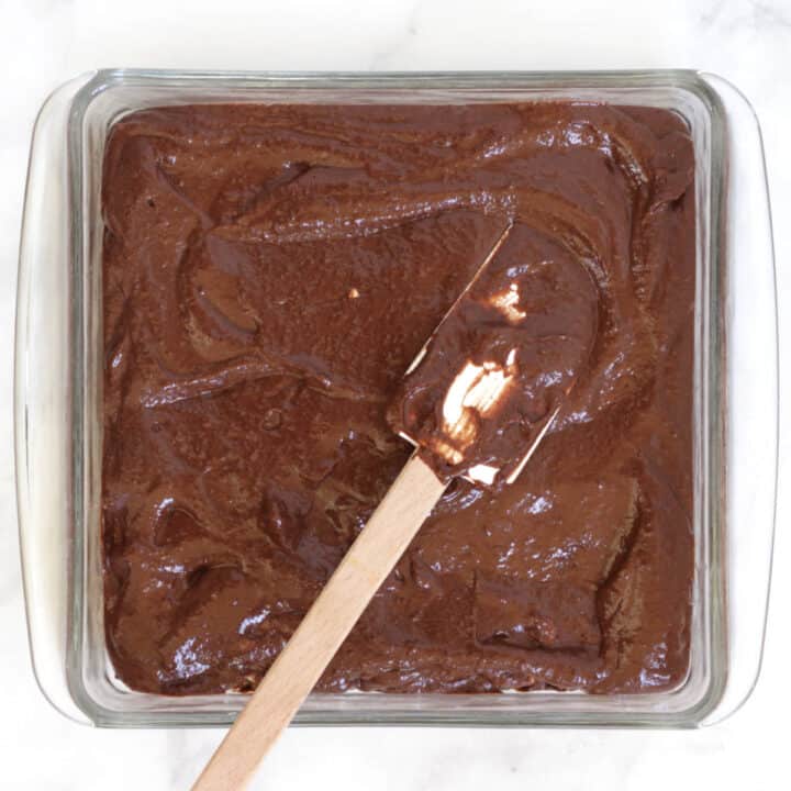 chocolate batter being smoothed into a square pyrex cake pan with spatula