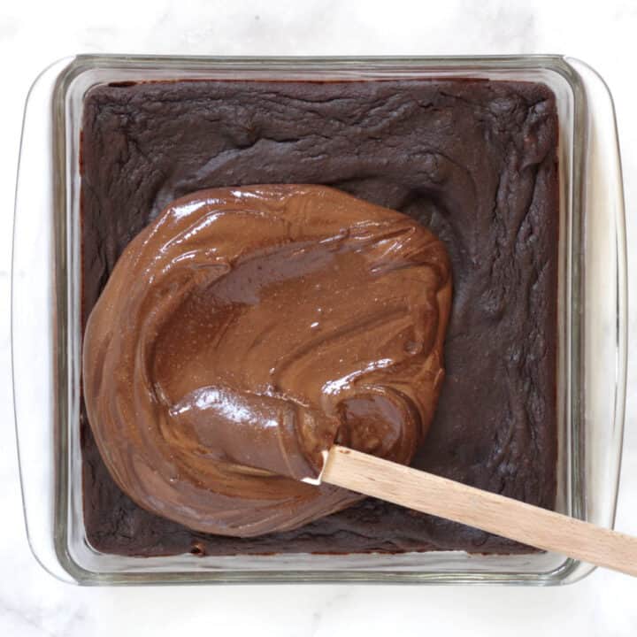 chocolate frosting being spread over baked brownies