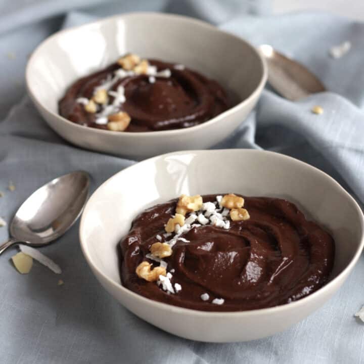 two bowls of chocolate pudding sprinkled with coconut flakes and chopped nuts