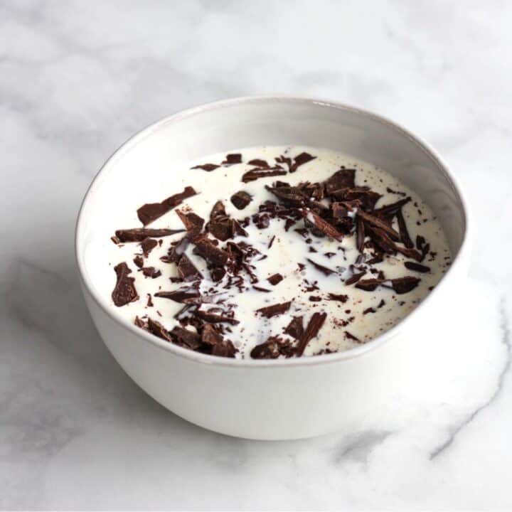 chopped chocolate sits surrounded by cream in a white bowl