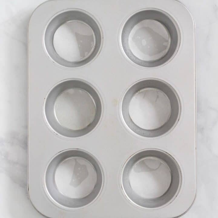 looking into 6-cup muffin pan with round cutouts of parchment paper lining the bottom of each cup