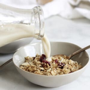 milk pouring from glass bottle onto bowl of granola