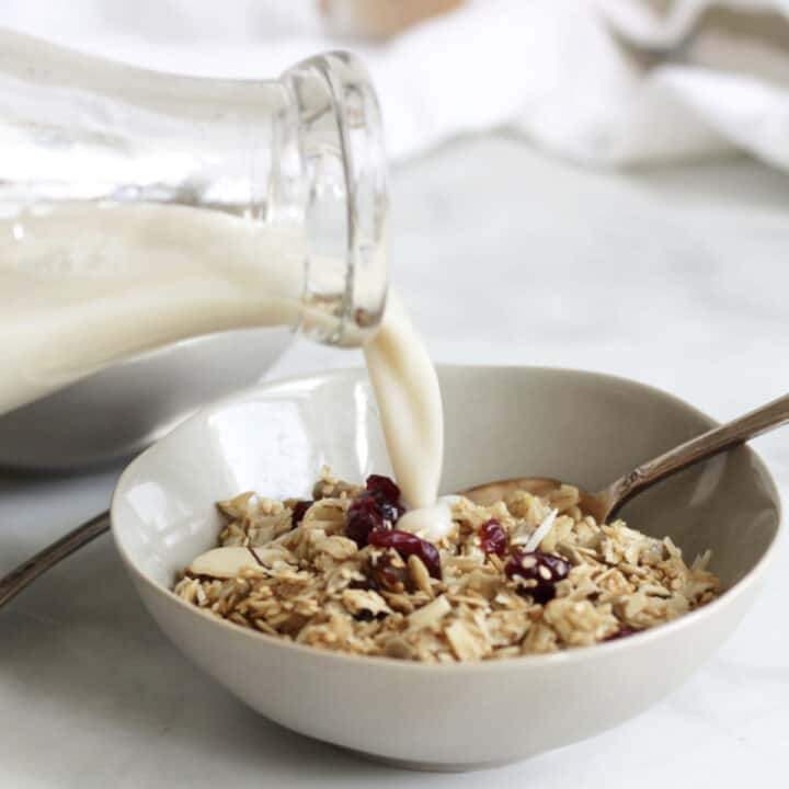 milk pouring from glass bottle onto bowl of granola