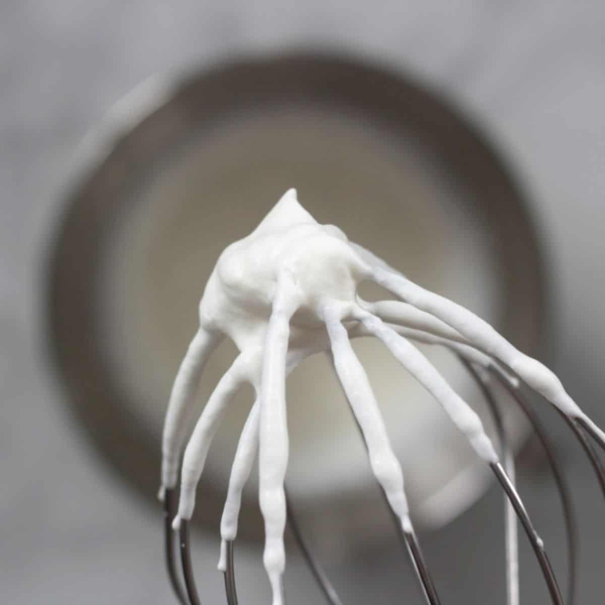 closeup of stiffly beaten whipped cream on whisk held over bowl