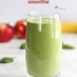 glass filled with a fresh, green smoothie, apples, banana, and spinach leaves in background