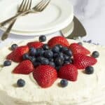 round layer cake decorated with white frosting, strawberries, and blueberries.