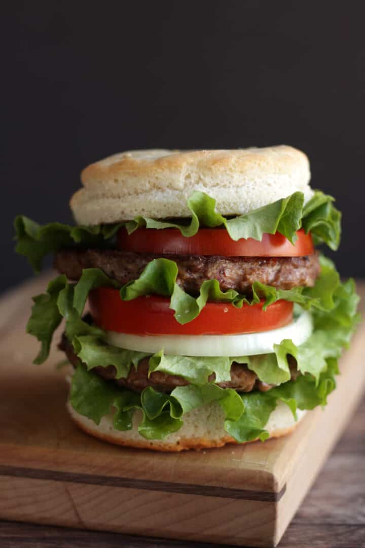 tall, stacked hamburger with tomato, onion, and lettuce in gluten free bun