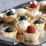 mini tarts each topped with a berry or whipped cream, sitting on a silver platter