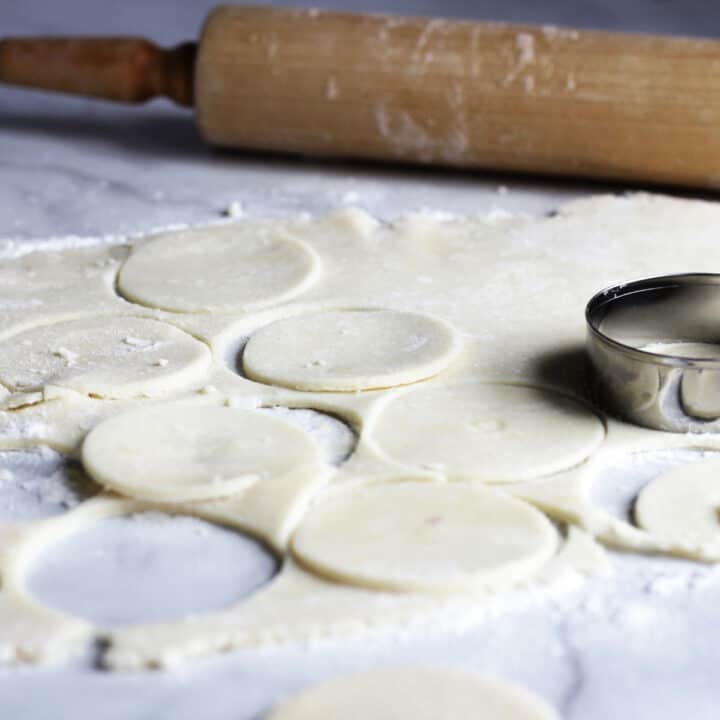 rounds of pastry being cut on marble surface, with wooden rolling pin in background
