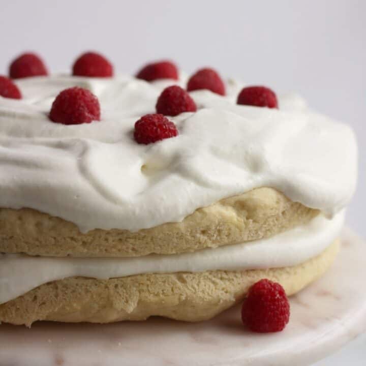 two round layers of gluten free vanilla cake topped with whipped cream and raspberries