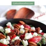 bowl of strawberry spinach salad with wooden tongs in background