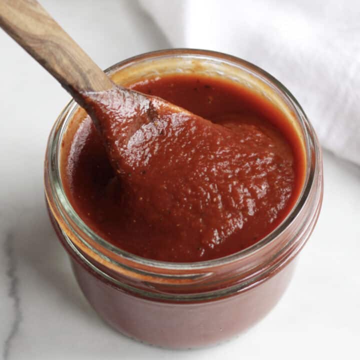 shimmering red barbecue sauce in a jar with a wooden spoon