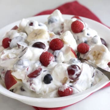 berries, grapes, apple and banana chunks in whipped cream in white bowl