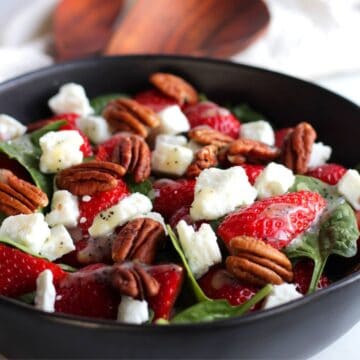 salad with strawberries, spinach, pecans, and feta cheese in black bowl