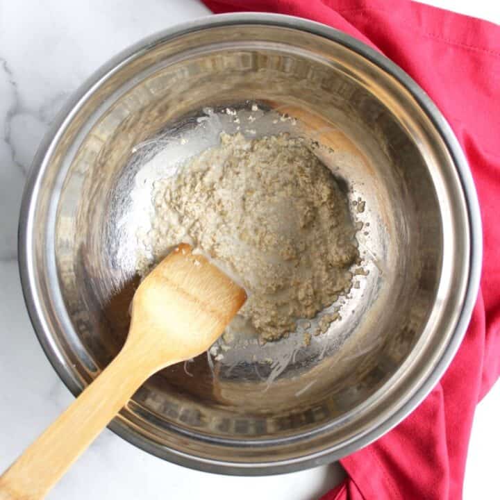 oats in milk in bottom of stainless steel mixing bowl with wood spatula