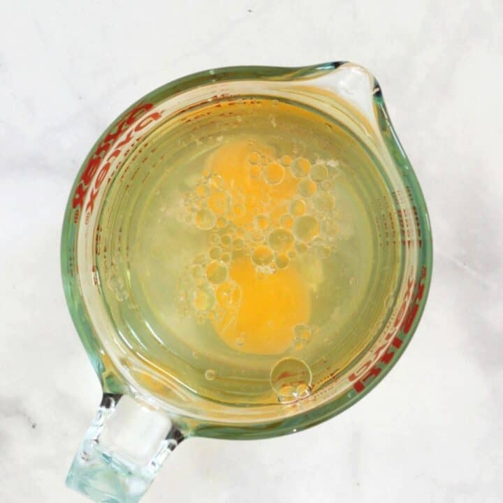 two egg yolks with watery liquid in pyrex measuring cup