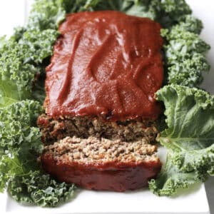 meatloaf topped with barbecue sauce, and one sliced lying down, resting in bed of kale