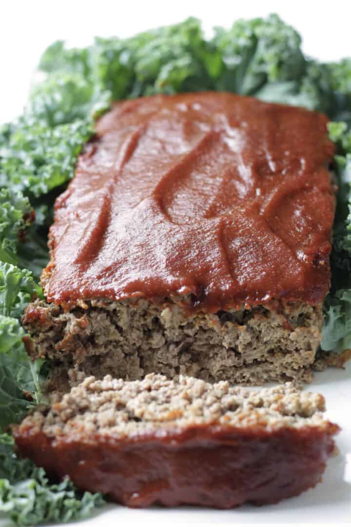 gluten free meatloaf with barbecue sauce on top and one end sliced off, surrounded by greens