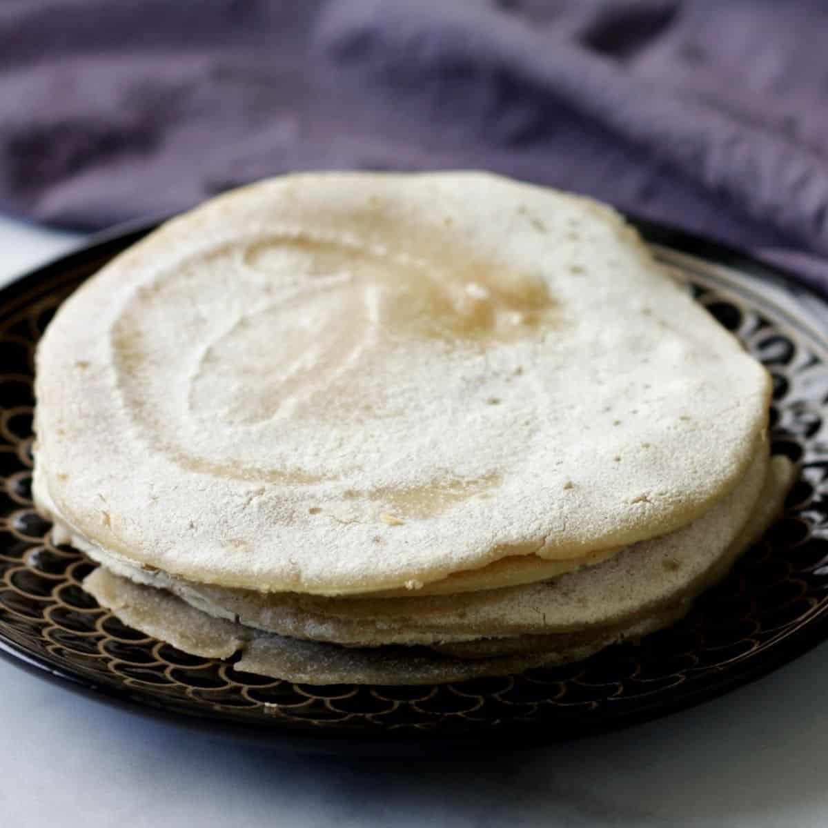 stack of flour tortillas on black plate with lavender napkin in background