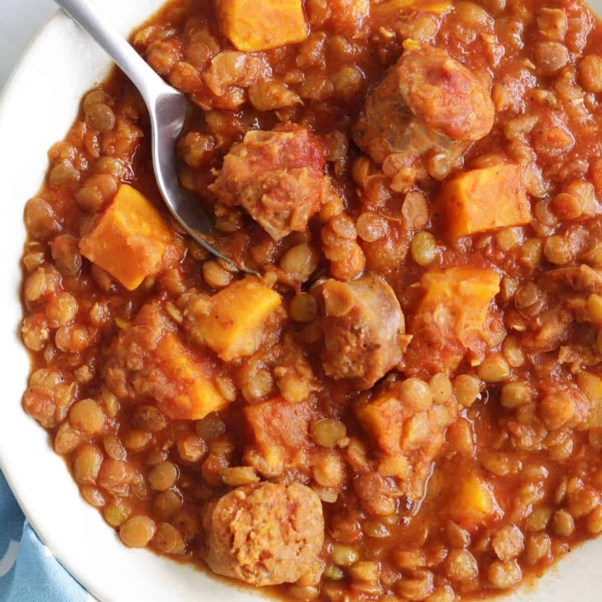 closeup of lentils in tomato sauce with chunks of sausage and sweet potato