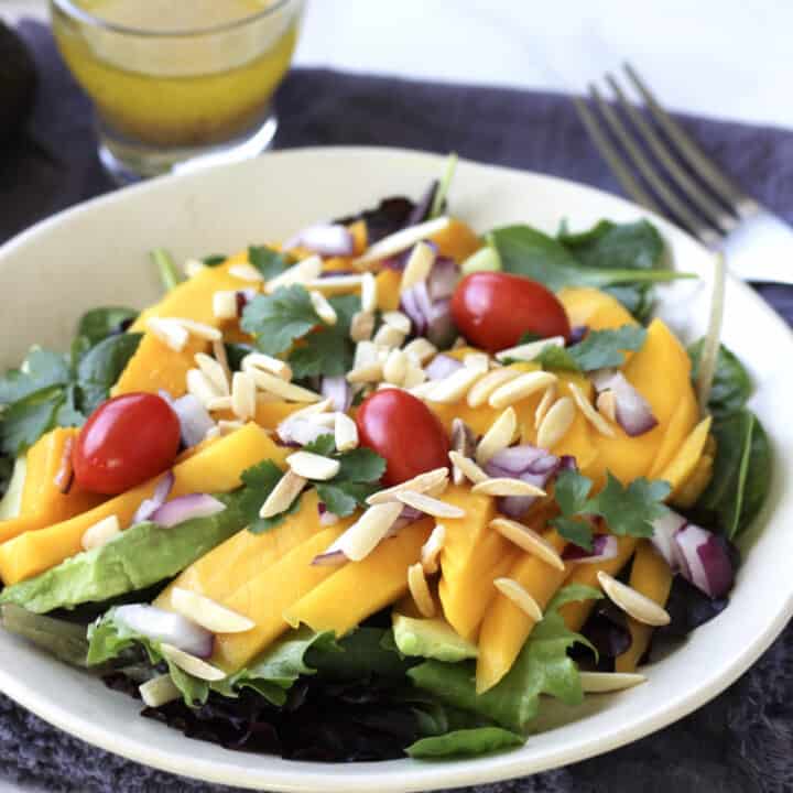 grape tomatoes, slivered almonds, cilantro, sliced mangos and avocados on lettuce leaves in a shallow white bowl