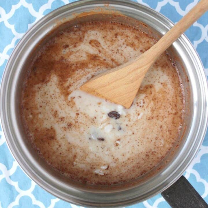 milky mixture with a couple raisins and cinnamon sprinkled on top, in stainless saucepan with wooden spoon.