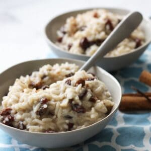 two bowls of creamy rice pudding with raisins on blue placemat.