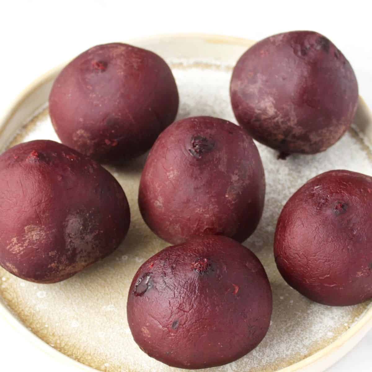 Six cooked, unpeeled beets on a beige plate