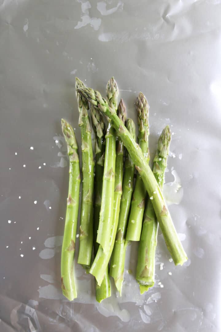 asparagus spears tossed in oil and coarse salt lying on a sheet of aluminum foil.