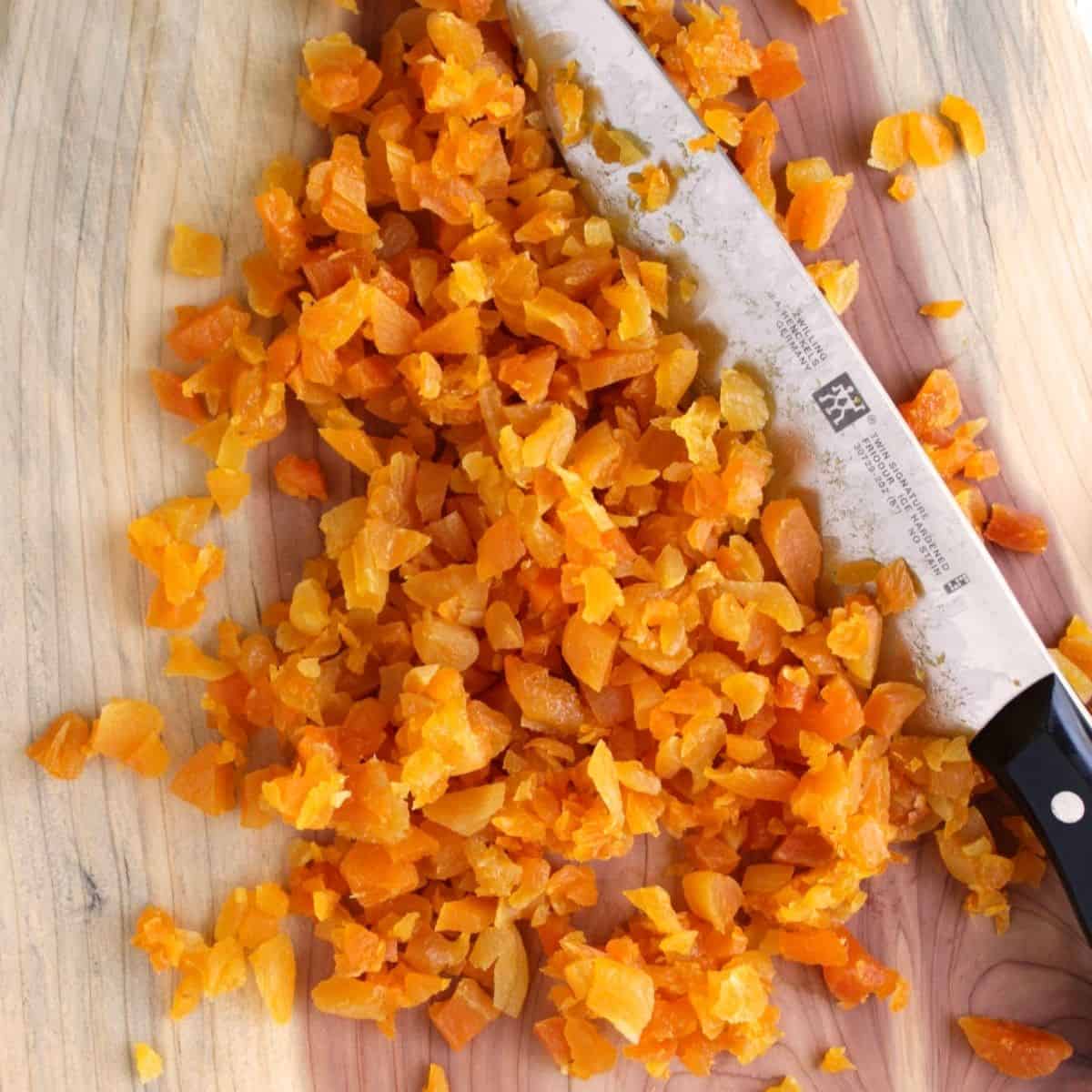 chopped dried apricots on wooden board with knife.