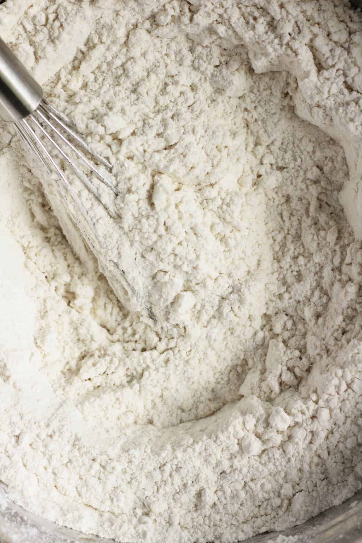 closeup of white flour with a whisk in it.