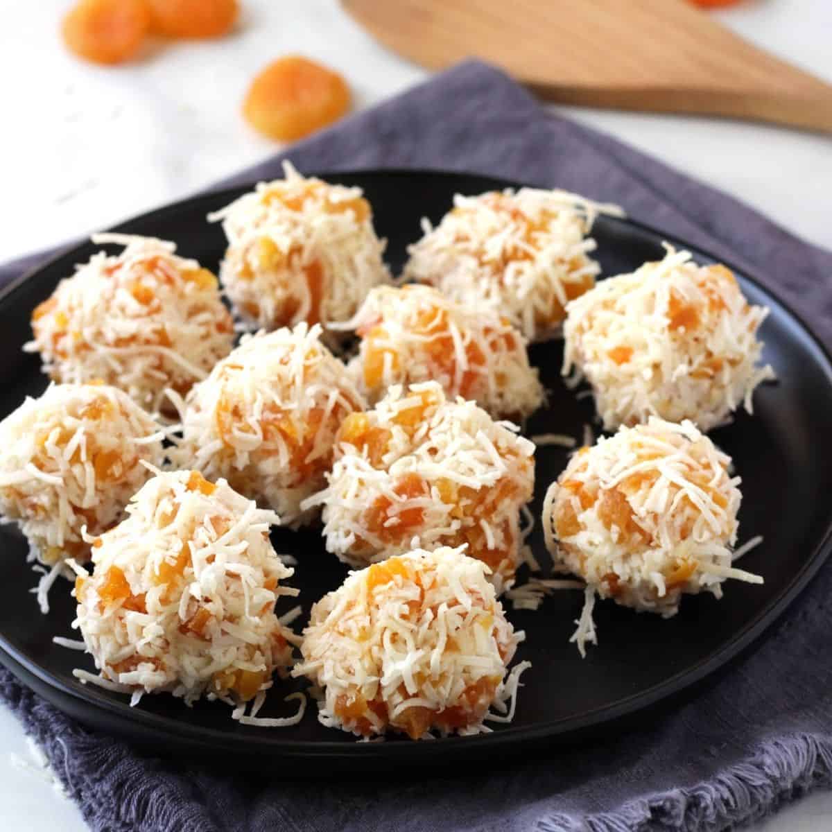 balls of apricot and shredded coconut sit on a black plate.