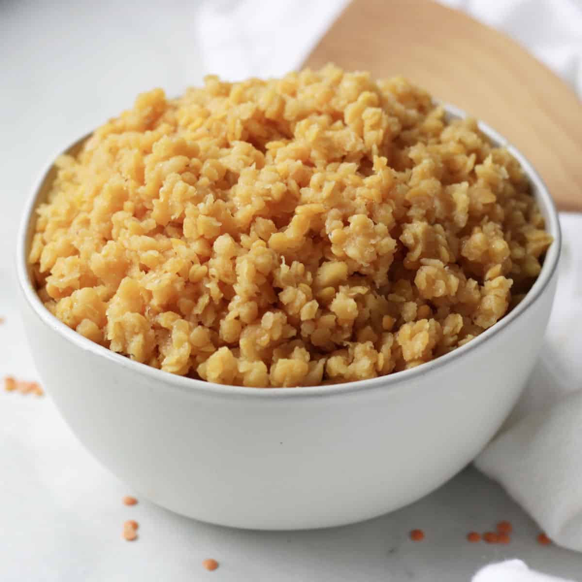 golden coloured cooked red lentils piled high in a white bowl.