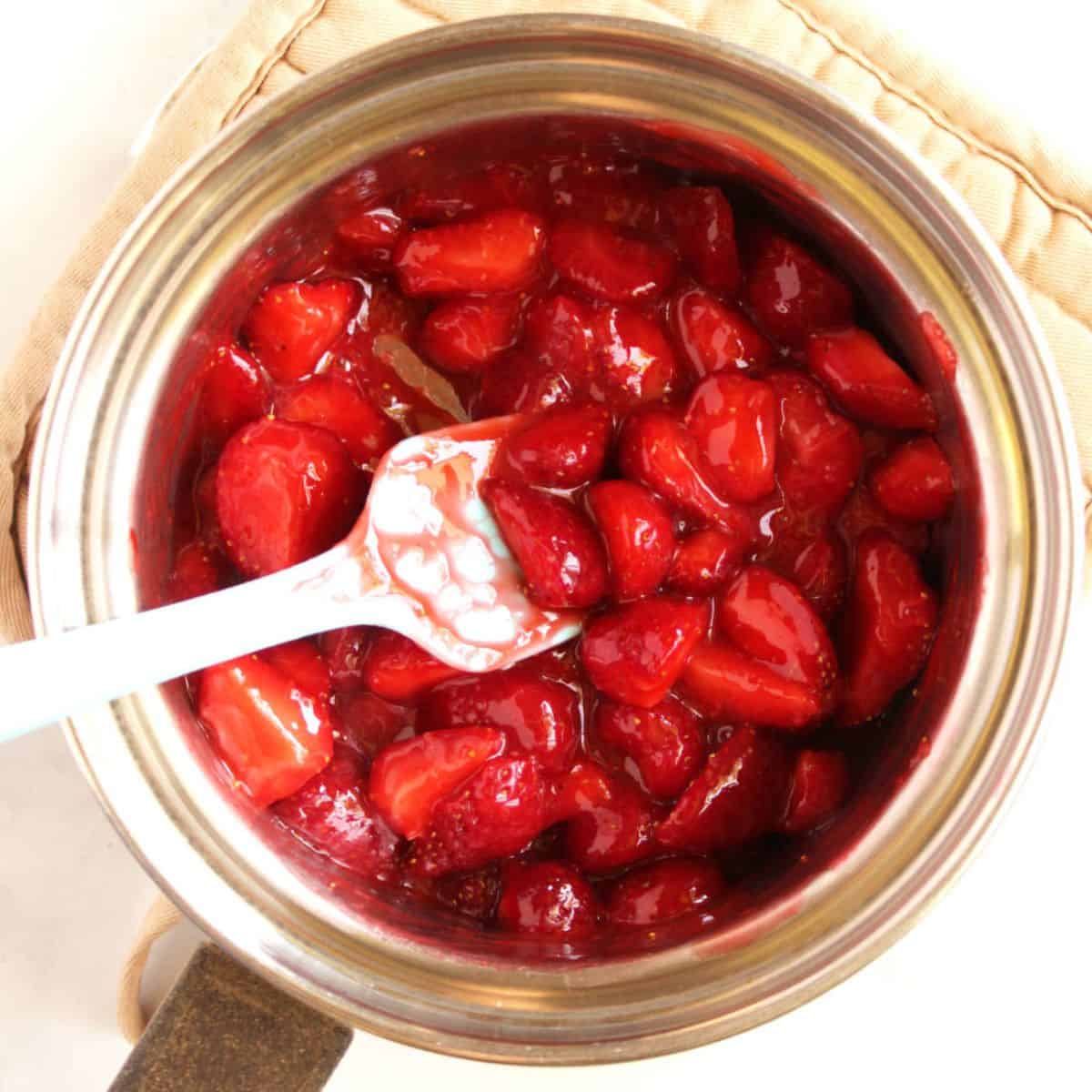 pale spatula stirs partially cooked strawberries